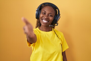 African american woman listening to music using headphones smiling friendly offering handshake as greeting and welcoming. successful business.