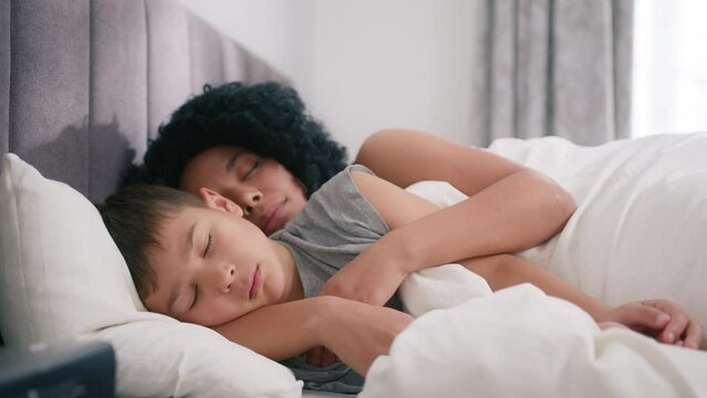 Happy African American single mother with little child lying on bed and sleeping together during day time. Portrait of young afro woman hugging preschool boy lying together in bedroom, motherhood time