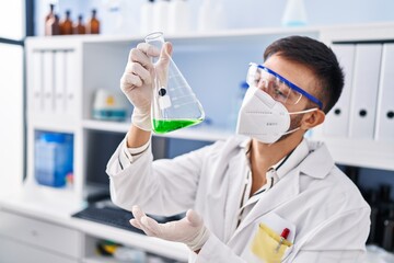 Young hispanic man scientist wearing medical mask holding test tube at laboratory