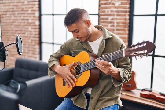 Young hispanic man musician playing classical guitar at music studio