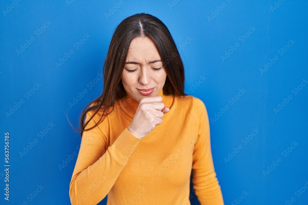 Poster Young brunette woman standing over blue background feeling unwell and coughing as symptom for cold or bronchitis. health care concept.