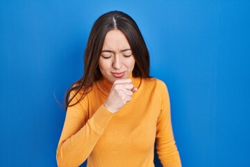 Obraz premium Young brunette woman standing over blue background feeling unwell and coughing as symptom for cold or bronchitis. health care concept.