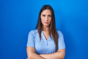 Young brunette woman standing over blue background skeptic and nervous, disapproving expression on...