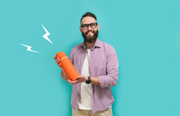 Young bearded charismatic hipster guy advertises, presents a thermos on a blue studio background