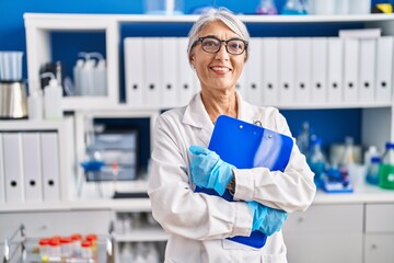 Middle age grey-haired woman scientist smiling confident holding clipboard at laboratory