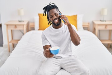 African american woman talking on the smartphone drinking coffee at bedroom