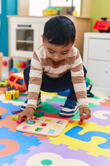 Adorable hispanic toddler playing with maths puzzle game sitting on floor at kindergarten