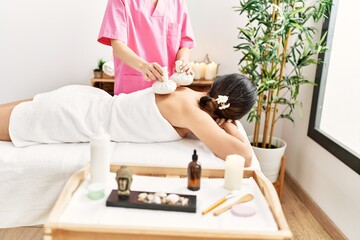 Obraz na płótnie Canvas Middle age hispanic woman having back massage using thai bags at beauty center