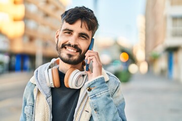 Young hispanic man talking on the smartphone wearing headphones at street