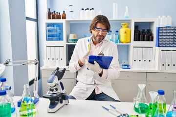 Middle age man scientist holding test tube reading document at laboratory