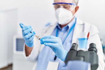 Middle age grey-haired man wearing scientist uniform using syringe at laboratory