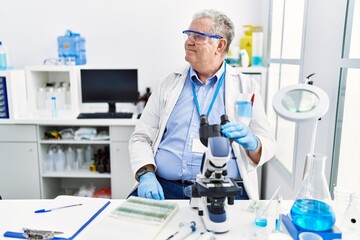 Fototapeta premium Senior caucasian man working at scientist laboratory looking away to side with smile on face, natural expression. laughing confident.
