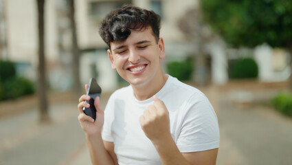 Non binary man using smartphone with winner expression at park