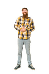 Fototapeta premium Young adult redhead man with a long beard standing full body isolated touches tummy, smiles gently, eating and satisfaction concept.