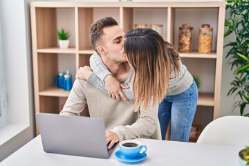 Man and woman couple using laptop hugging each other and kissing at home