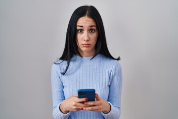 Hispanic woman using smartphone skeptic and nervous, frowning upset because of problem. negative...