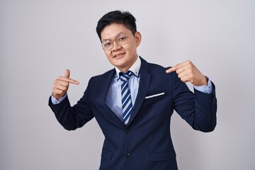 Young asian man wearing business suit and tie looking confident with smile on face, pointing oneself with fingers proud and happy.