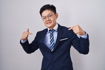 Young asian man wearing business suit and tie looking confident with smile on face, pointing...