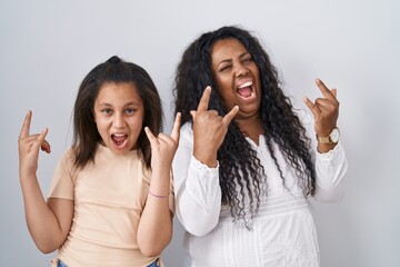 Mother and young daughter standing over white background shouting with crazy expression doing rock symbol with hands up. music star. heavy music concept.