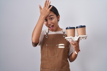 Young hispanic woman wearing professional waitress apron holding coffee surprised with hand on head...