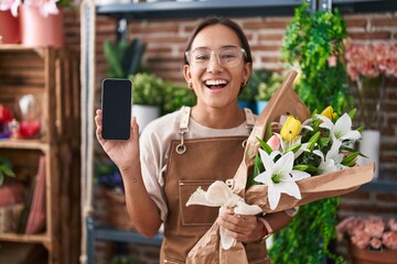 Young hispanic woman working at florist shop showing smartphone screen smiling and laughing hard out loud because funny crazy joke.