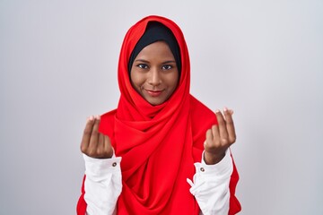 Young arab woman wearing traditional islamic hijab scarf doing money gesture with hands, asking for salary payment, millionaire business