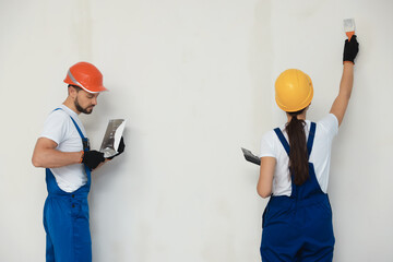 Professional workers plastering wall with putty knives in hard hats
