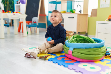 Adorable hispanic boy playing with ball sitting on floor at kindergarten