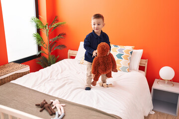 Adorable hispanic boy holding monkey doll standing on bed at bedroom