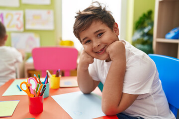 Adorable hispanic boy student smiling confident sitting on table at kindergarten