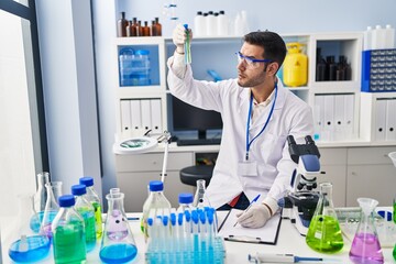 Fototapeta premium Young hispanic man scientist holding test tubes writing report at laboratory