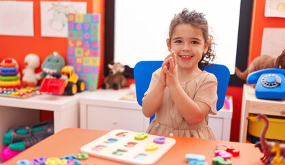 Adorable hispanic girl playing with maths puzzle game clapping hands at kindergarten