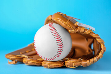 Catcher's mitt and baseball ball on light blue background, closeup. Sports game
