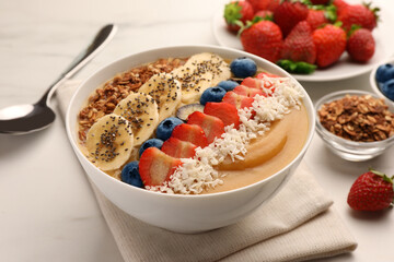Delicious smoothie bowl with fresh berries, banana, coconut flakes and granola on white table, closeup
