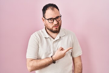 Plus size hispanic man with beard standing over pink background pointing aside worried and nervous...