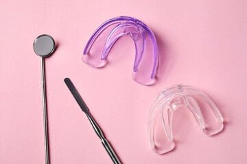 Bite correction. Transparent mouth guards and dentist tools on light pink background, flat lay