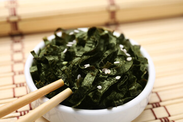 Chopped nori sheets with sesame and chopsticks on bamboo mat, closeup