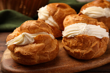 Delicious profiteroles with cream filling on wooden table, closeup