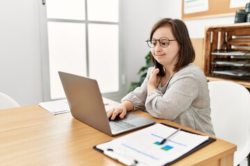 Brunette woman with down syndrome working using laptop speaking on the phone at business office