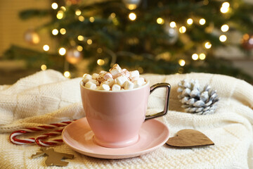 Obraz na płótnie Canvas Cup of tasty cocoa with marshmallows, candy canes and Christmas decor on knitted plaid indoors
