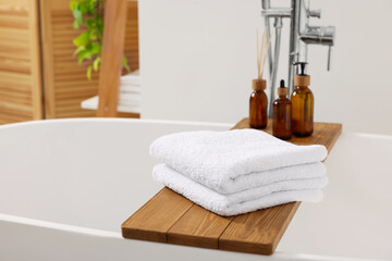Fototapeta na wymiar Stacked soft towels on tub tray in bathroom