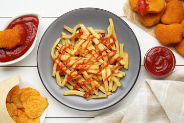 Tasty french fries, chicken nuggets and chips with ketchup served on white wooden table, flat lay