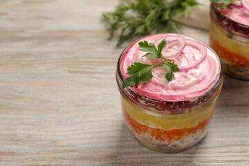 Glass jars of herring under fur coat on wooden table, space for text. Traditional Russian salad