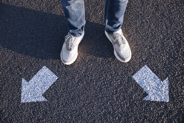 Choice of way. Man standing in front of drawn marks on road, closeup. White arrows pointing in...