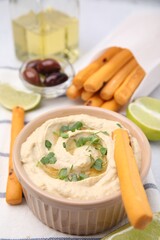 Delicious hummus with grissini sticks on light grey table, closeup