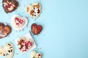 Tasty chocolate heart shaped candies with nuts on light blue background, flat lay. Space for text