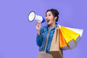 Young beautiful asian woman announces with a voice about promotions  at a discounted price over violet background. . Shopping and fashion concept.Shout out loud with megaphone.