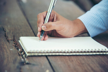 Man hands writing notebook diary with coffee cup and smartphone on wood desk. Close up man hands...