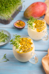 Mango yogurt with passionfruit and cilantro microgreen in glass on blue. Side view, selective focus.