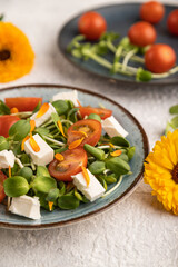 Vegetarian salad of tomatoes, marigold, microgreen, feta cheese on gray. Side view, selective focus.